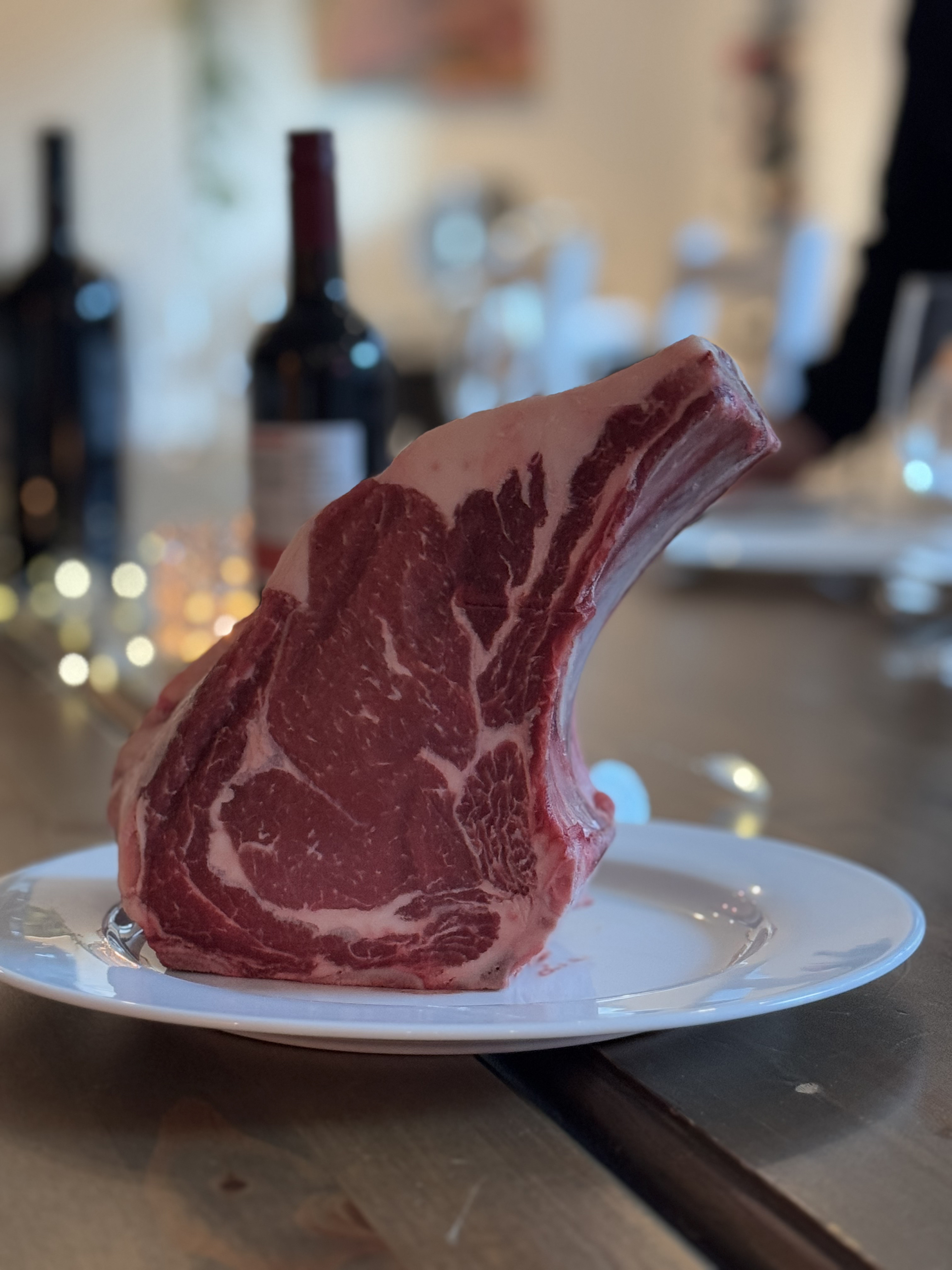 Marmoriertes Premium-Tomahawk auf einem Teller, im Hintergrund Wein und Kerzenlicht